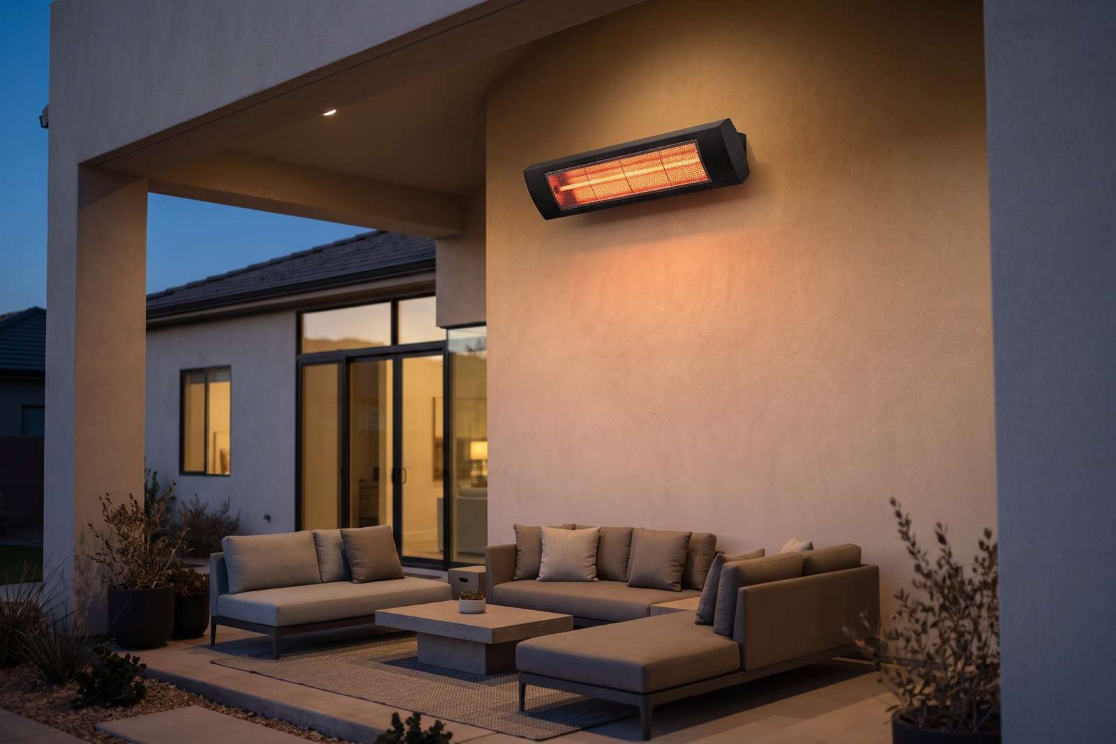A black wall-mounted gas patio heater with a glowing ceramic face on a stucco wall above a covered patio seating area at dusk.