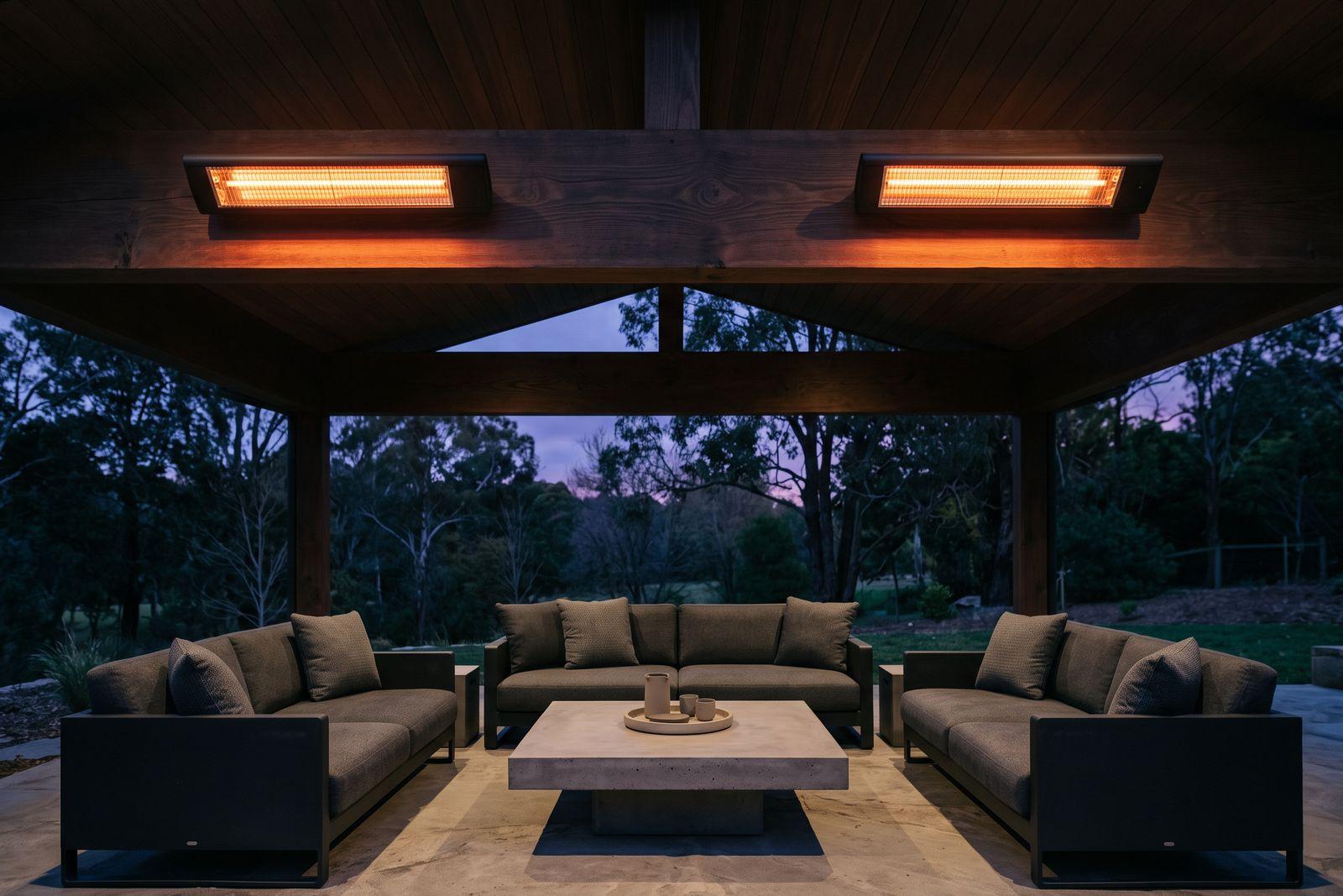 Two matte-black electric infrared heaters mounted on the beam of a covered outdoor lounge at dusk, both glowing.