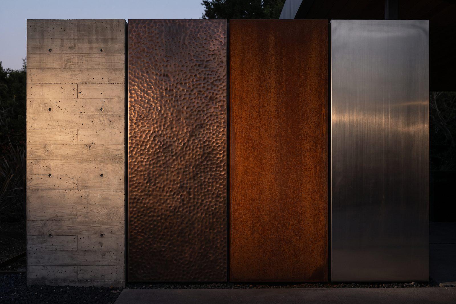 Four material surfaces side by side in warm raking light: board-formed concrete, hammered copper, rust-brown weathered corten and brushed stainless steel.